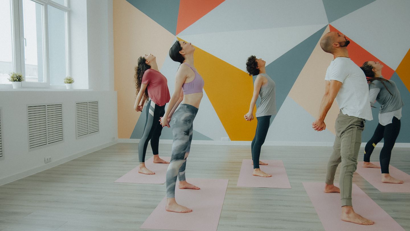 A group of adults practicing yoga in a modern indoor studio with geometric wall design.